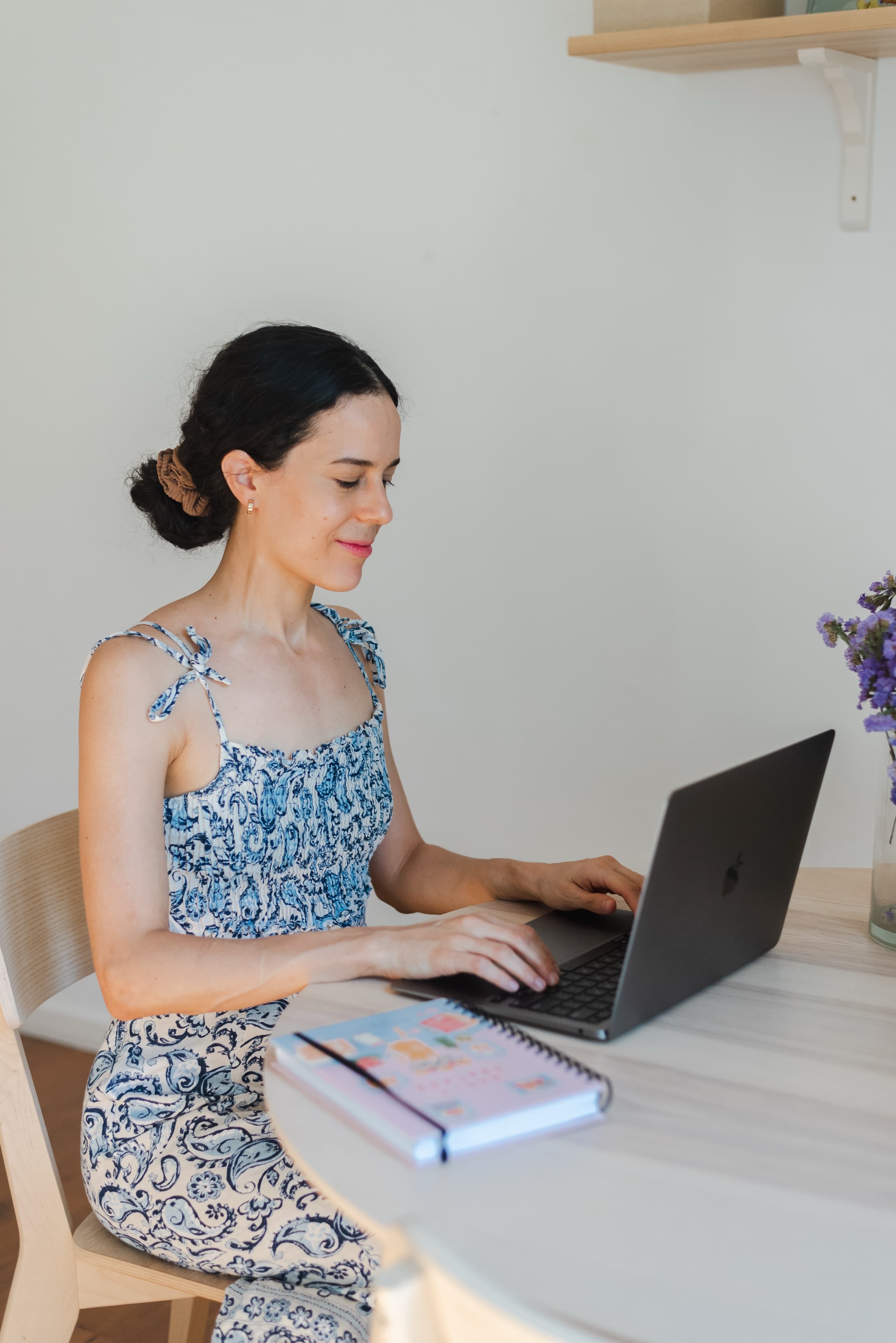 Julieta Benedetti sonriendo mientras trabaja en su laptop, sentada a una mesa de madera clara.